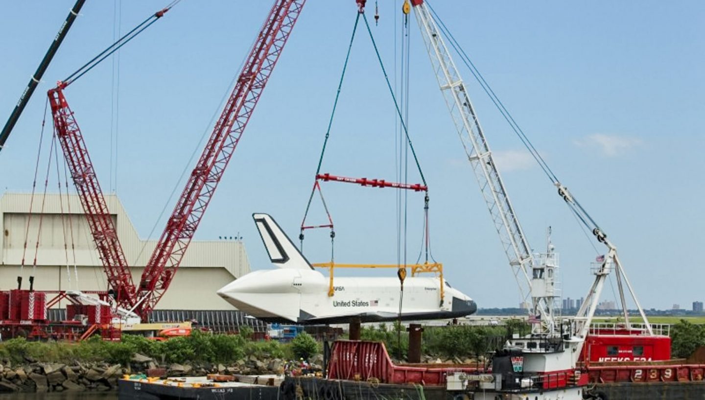 Cranes lifting space shuttle onto river platform